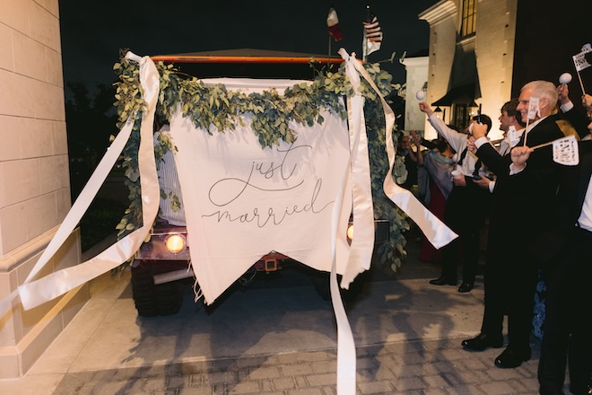 A fabric "Just Married" sign decorated with greenery on the back of a vehicle. 