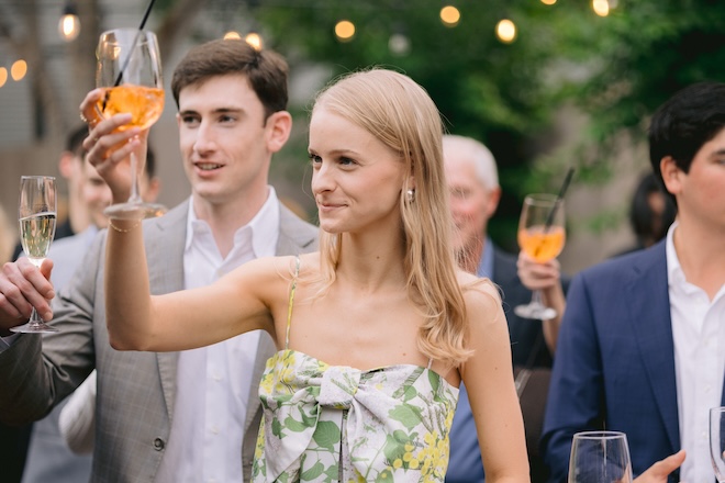 The birde raising an aperol spritz and the groom raising a glass of champagne at their rehearsal dinner.