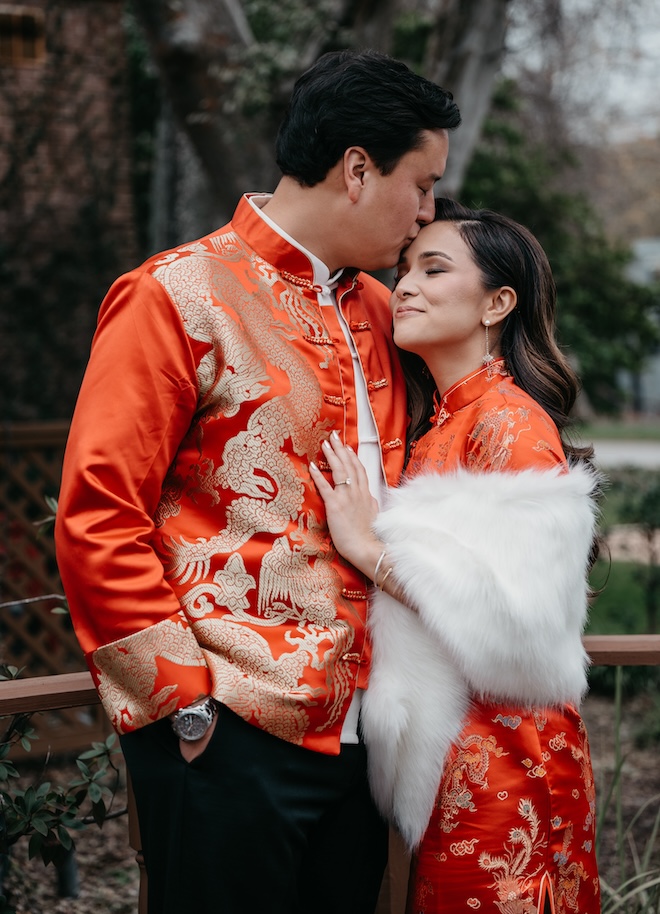 A groom kissing his bride on the forehead wearing traditional red garments. 