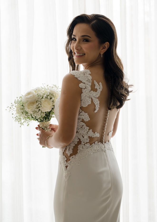 The bride smiling while showing the back of her wedding dress with lace detailing and white buttons. 