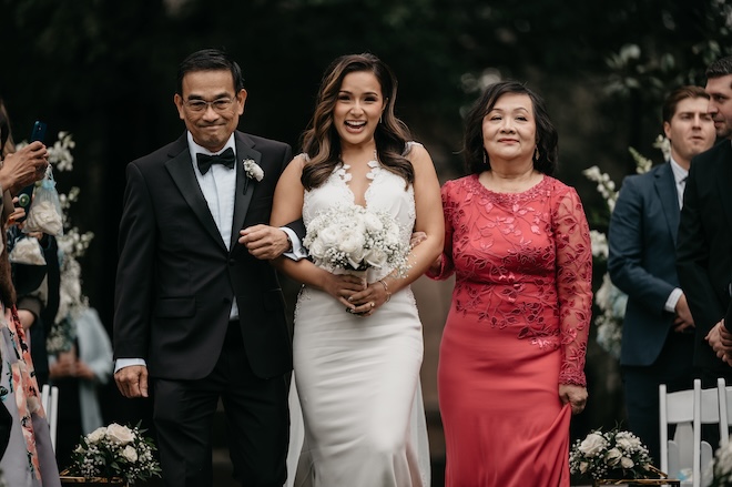 The bride walking down the aisle with both of her parents next to her. 