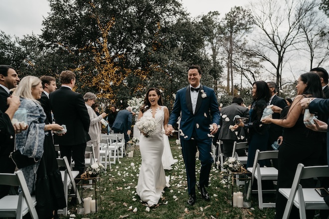 The bride and groom holding hands walking back down the aisle with flower petals being thrown. 