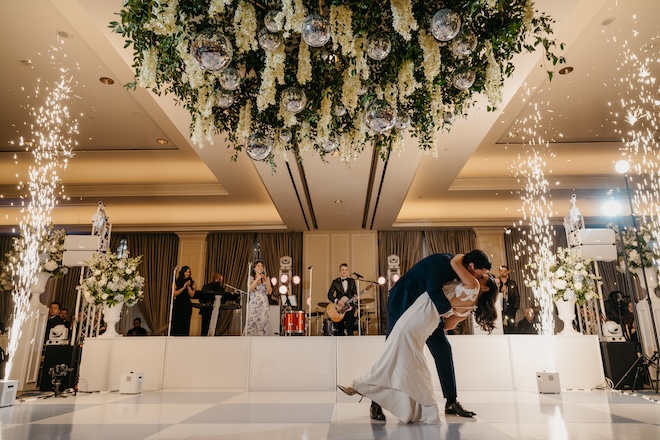 The groom dipping the bride on the blue and white checkered dance floor with sparklers behind them. 