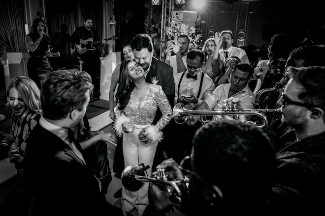 The bride in a jumpsuit dancing with the groom next to the band. 