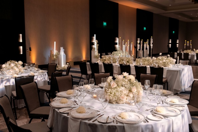 White reception tables decorated with white florals, baby's breath and candles in the ballroom of Hyatt Regency Baytown-Houston. 