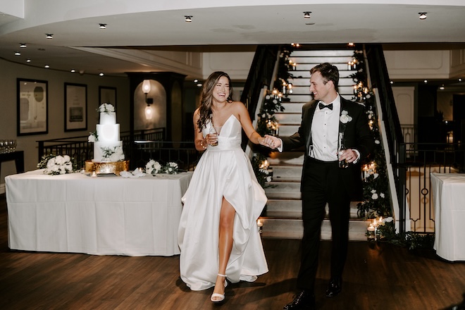 A bride and groom holding hands and smiling while entering the ballroom of the Magnolia Hotel Houston. 