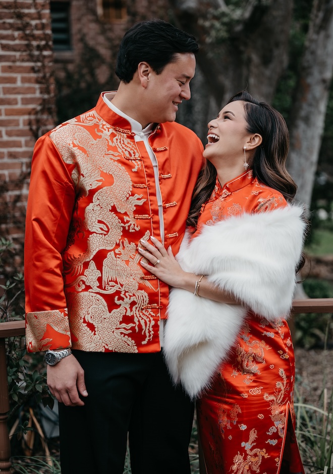 The bride and groom smile at each other while wearing traditional red garments. 