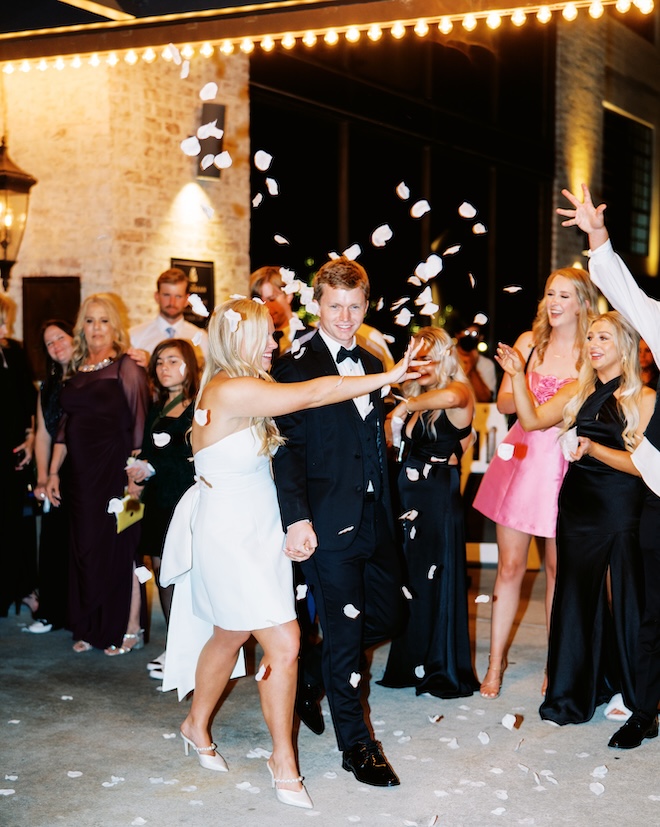 The bride and groom leaving the venue with white floral petals around them. 