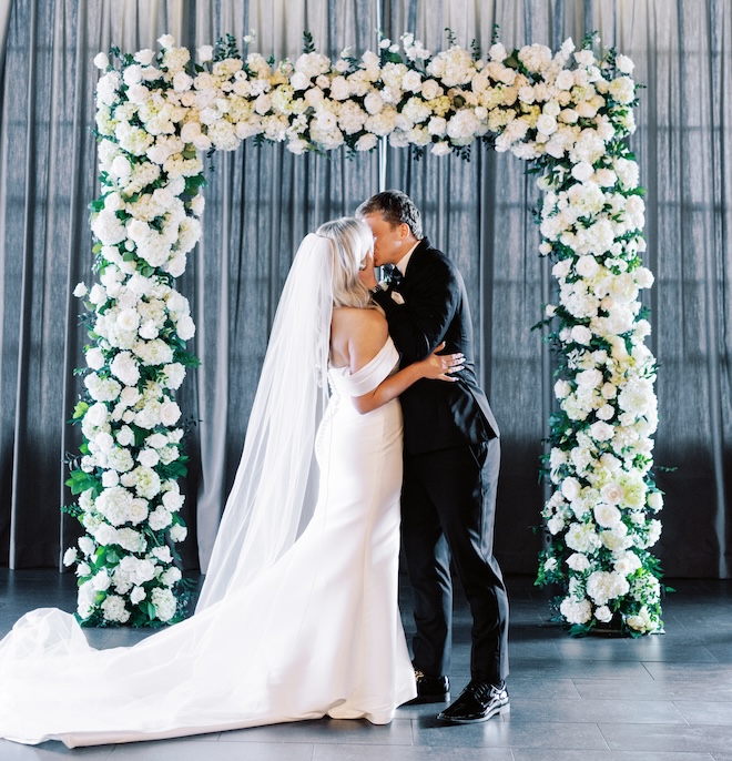 The bride and groom kissing at the white floral covered altar. 