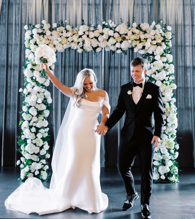 The bride and groom cheering at the white floral covered altar. 