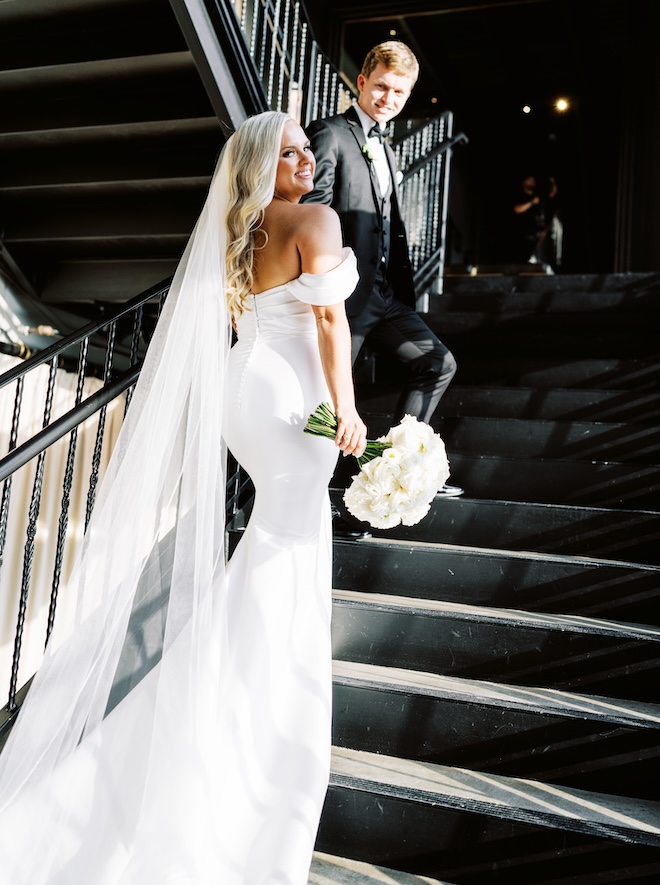 The groom holding the bride's hands and leading her up a black staircase. 