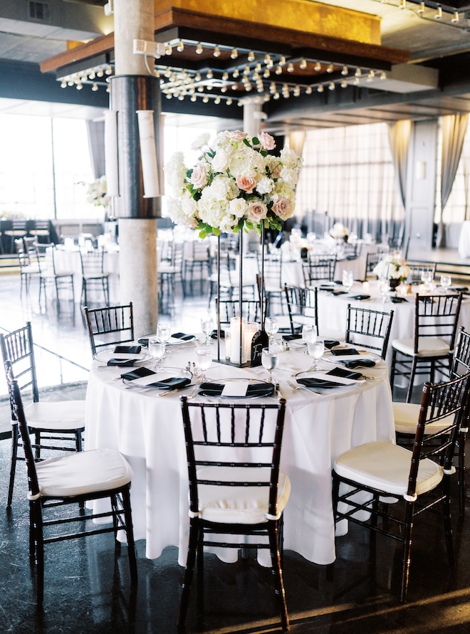 A reception table decorated with white and black linens and a white and blush floral centerpiece. 