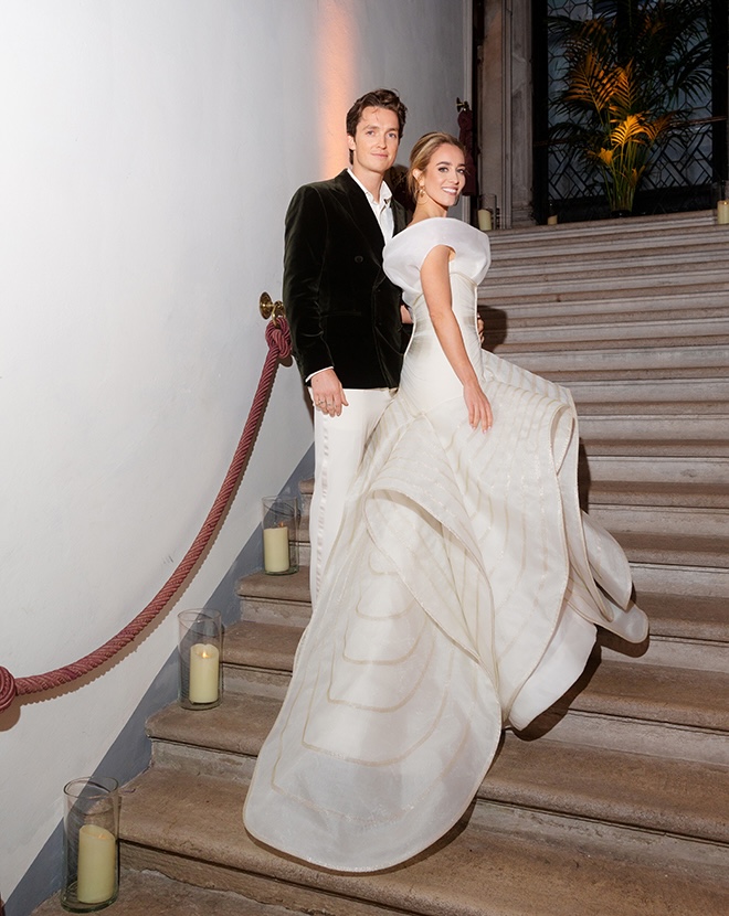 The couple stand on concrete stairs lined with pillar candles at their welcome dinner in Venice, Italy. 