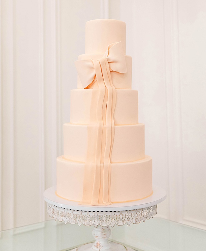 A five-tier peach colored wedding cake with a fondant bow by For Heaven's Cake. 