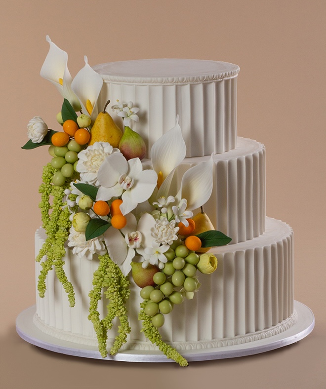 A three tier white wedding cake embellished in greenery, florals and fruit. 