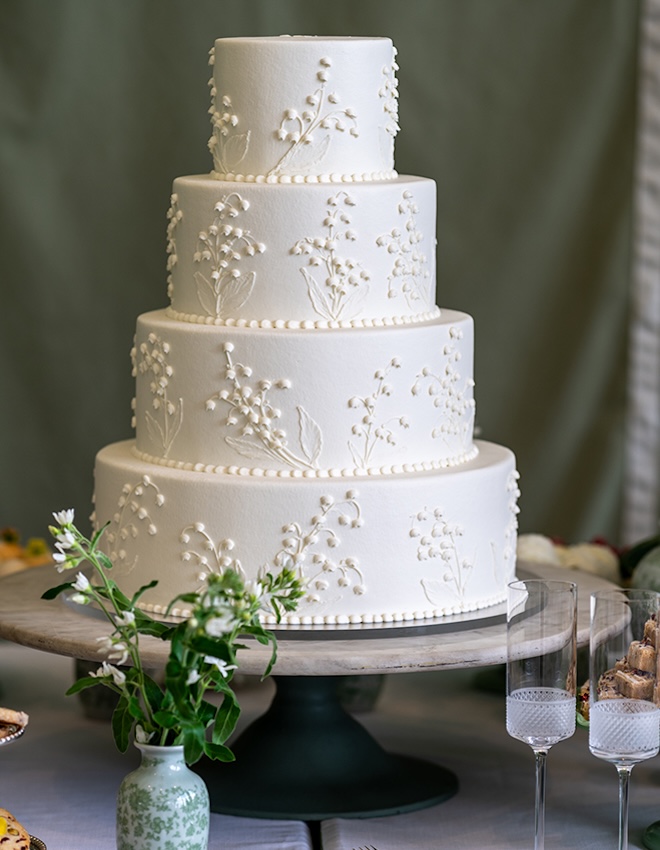 A four-tier white wedding cake with intricate piping of lilies of the valley by Susie's Cakes.