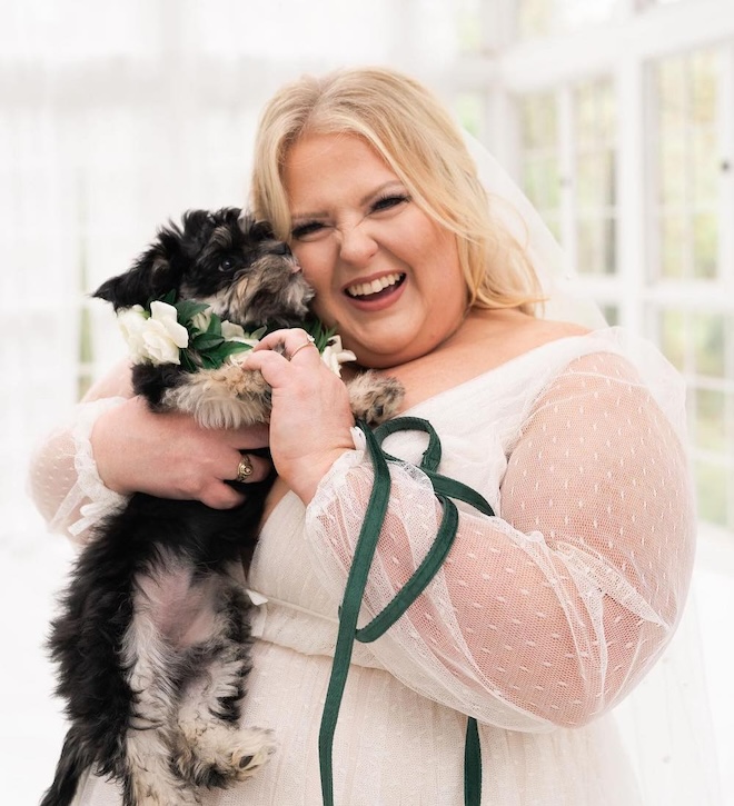 A bride smiling with a small dog on her wedding day. 