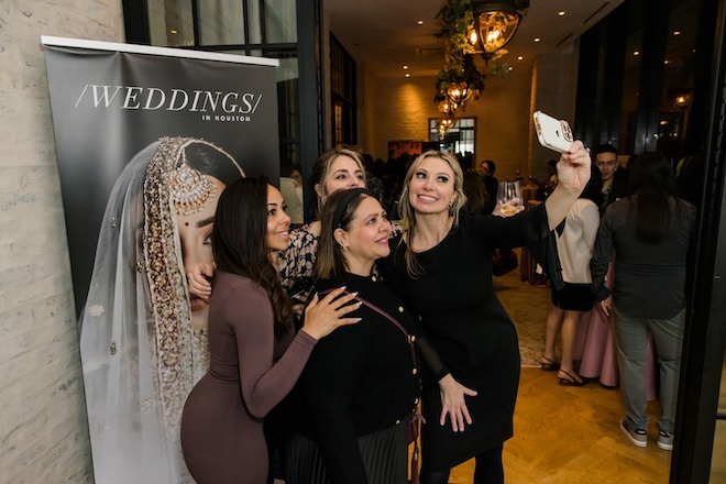 A group of women taking a selfie in front of a Weddings in Houston banner. 