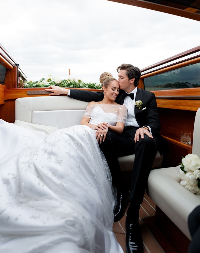 The groom kisses the bride on her forehead while they ride on a Riva yacht down the Venice canals. 