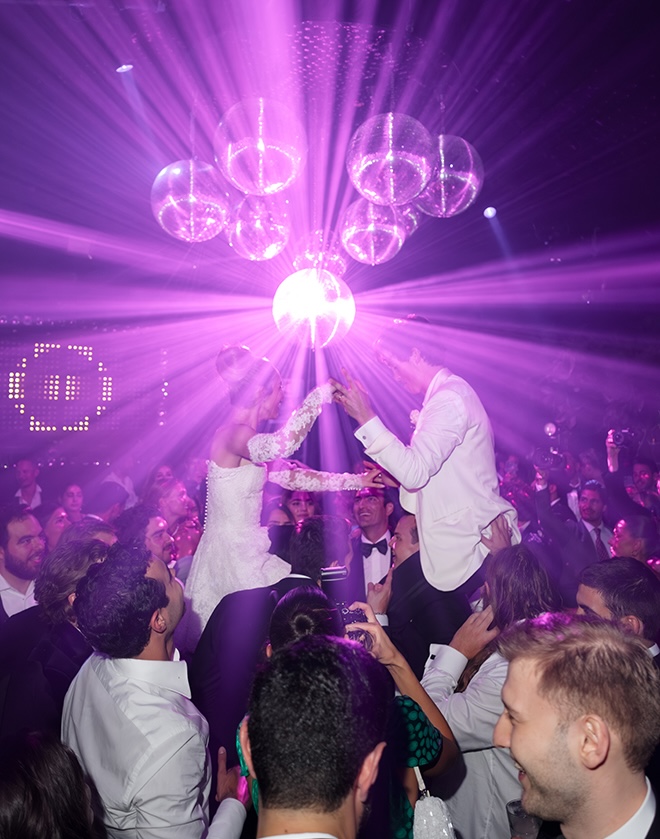 The couple sit on wedding guests shoulders under purple lights and disco balls at their after-party. 