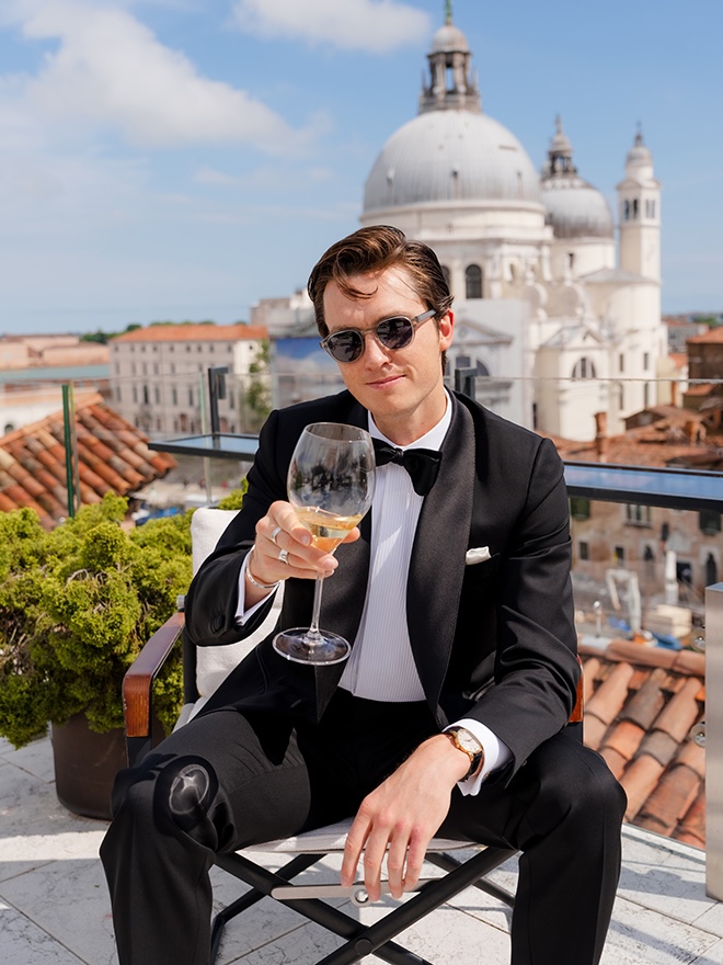 The groom drinks a glass of white wine on the balcony overlooking the Venetian Market.